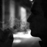 Czarno-białe zdjęcie zacienionej twarzy i ręki człowieka podczas palenia